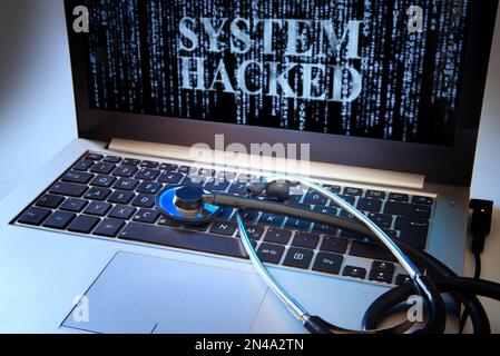 Laptop mit blauer Matrix und NACHRICHTENSYSTEM, DAS ALS Symbol für Cyberkriminalität AUF dem Bildschirm GEHACKT wurde, Stethoskop auf der Tastatur, Konzept für Netzwerksicherheit, Daten Stockfoto