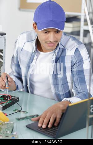 Mann, der ein Notebook benutzt, um einen pc zu reparieren Stockfoto