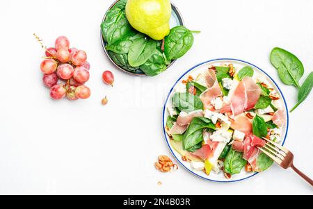 Köstlicher Birnensalat mit Jamon, Blauschimmelkäse, Spinat und Walnüssen auf weißem Tischhintergrund, Blick von oben Stockfoto