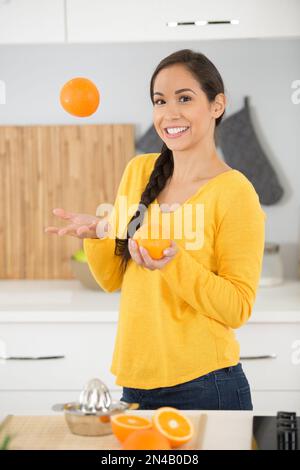 Schöne Frau jongliert mit Orangen in ihrer Küche Stockfoto