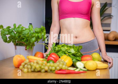 Frau in einem kurzen Sporttop, die hinter einem Tisch mit Gemüse und Obst steht Stockfoto