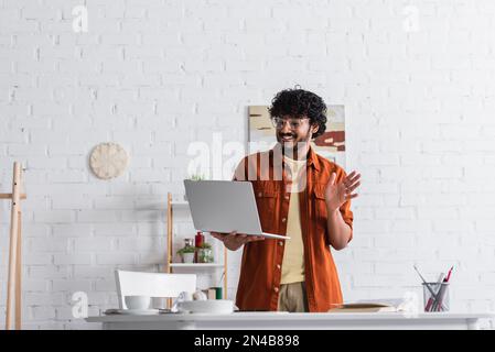 Fröhlicher indischer Freiberufler, der Video-Chat auf dem Laptop im Wohnzimmer hat, Stock Image Stockfoto
