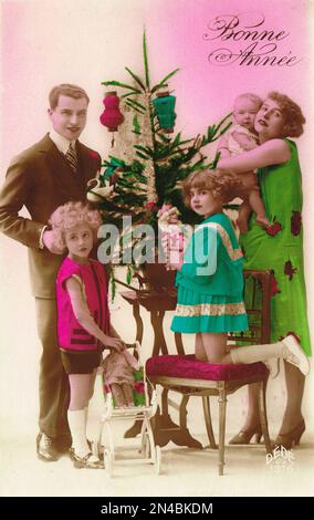 Edwardianische Ära Belle Epoque Französische Neujahrsgrüße Postkarte mit einer jungen Familie um einen Weihnachtsbaum herum. Ungefähr 1910 Stockfoto