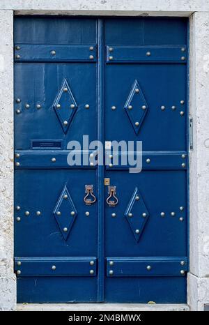 Vertikal: Antike, mittelalterliche blaue Tür mit Messing-Türgriffen glänzende Metallniete Altstadt Lissabon, Portugal Stockfoto