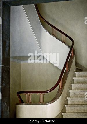 Vertikal: Art déco-Treppe und Geländer mit Marmortreppen, gebogenen Treppen und wunderschönem Handlauf aus poliertem braunem Holz und Metall Stockfoto