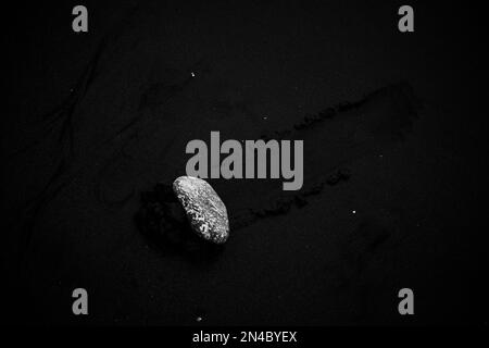 Eine Graustufenaufnahme von oben von einem Stein auf Sand. Stockfoto