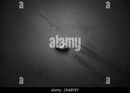 Eine Graustufenaufnahme von oben von einem Stein auf Sand. Stockfoto