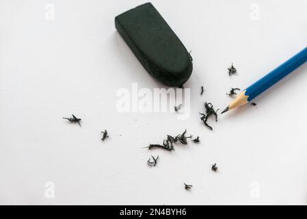 Blauer Bleistift, schwarzer Radierer und Schrott auf weißem Papierhintergrund. Stockfoto
