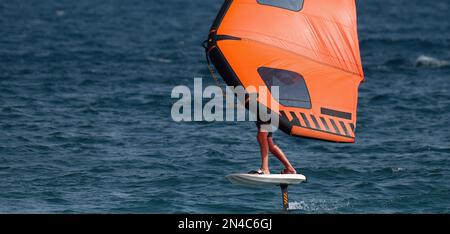 Ein Mann trägt Flügelfolien mit handgeführten aufblasbaren Flügeln und Tragflächensurfbrettern in einem blauen Ozean, reitet auf einem Windflügelbrett, surft auf den Wellen Stockfoto