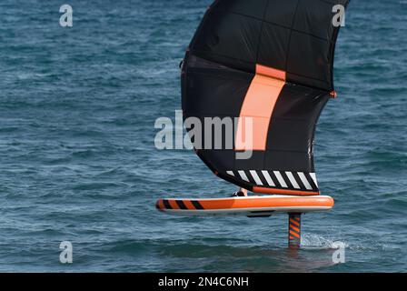 Ein Mann trägt Flügelfolien mit handgeführten aufblasbaren Flügeln und Tragflächensurfbrettern in einem blauen Ozean, reitet auf einem Windflügelbrett, surft auf den Wellen Stockfoto