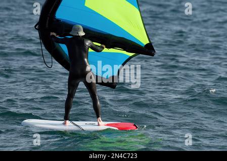 Ein Mann trägt Flügelfolien mit handgeführten aufblasbaren Flügeln und Tragflächensurfbrettern in einem blauen Ozean, reitet auf einem Windflügelbrett, surft auf den Wellen Stockfoto