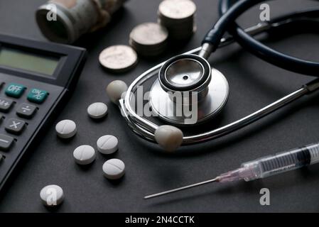 Konzept für Gesundheitsausgaben und Arztkosten. Stethoskop mit Pillen, Spritze, Taschenrechner, Geld und einem Haufen Münzen. Stockfoto