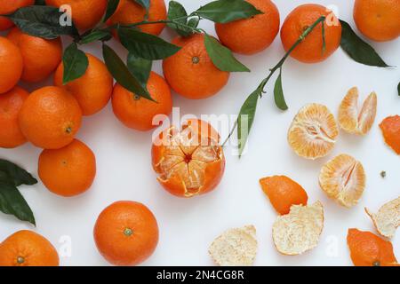 Mandarinen- und Clementinen-Zitrusfrüchte mit Blättern auf weißem Hintergrund, angeordnet mit Blättern, geschälten Früchten und verstreuter Schale und Fleisch, Draufsicht. Stockfoto