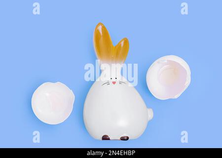 Ein geschlüpfter weißer Osterhasen und zerbrochene Eierschalen auf blauem Hintergrund. Ostern minimale kreative Komposition. Frohe Osterferien. Eine Grußkarte. Stockfoto