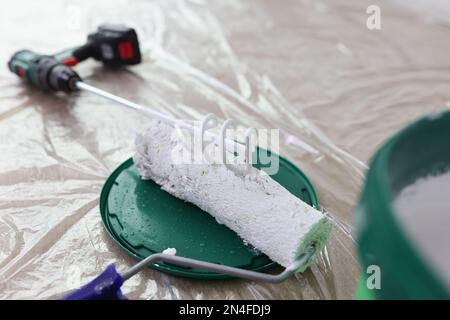 Lackmischer, Bürstenrolle und Eimer mit weißer Farbe auf überdachtem Boden. Stockfoto