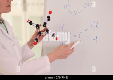 Chemikerin mit molekularem Modell und Zeichnen chemischer Formeln auf dem Whiteboard. Stockfoto