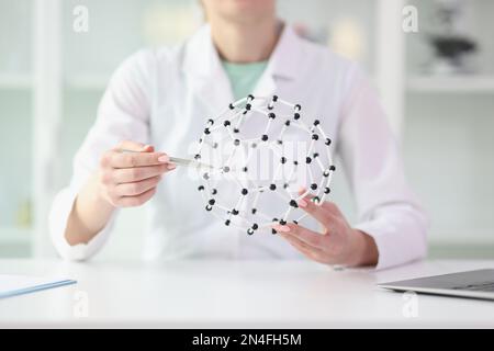 Eine Wissenschaftlerin zeigt ein Modell der Molekülstruktur in ihren Händen, sitzt am Labortisch. Stockfoto