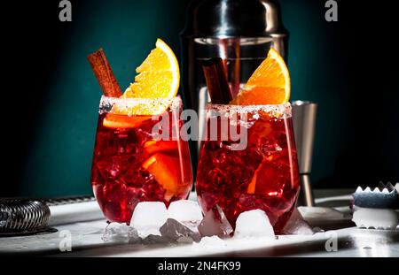 Negroni Mezcalito alkoholischer Cocktail mit Mezcal, Wermut, Bitter, Kräuterlikör, Orange, Zimt und Eis, dunkler Hintergrund, hartes Licht und Schatten Stockfoto
