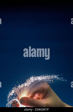 FRAUENHÄNDE HALTEN GLASFASERSTRÄNGE („OPTIK MAURER & SCHULTZ“ / „CORNING GLASS WORKS 1970“) ZWISCHEN DEN FINGERN Stockfoto