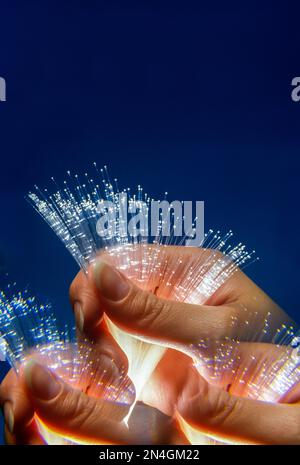 FRAUENHÄNDE HALTEN GLASFASERSTRÄNGE („OPTIK MAURER & SCHULTZ“ / „CORNING GLASS WORKS 1970“) ZWISCHEN DEN FINGERN Stockfoto