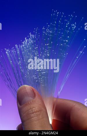 FRAUENHÄNDE HALTEN GLASFASERSTRÄNGE („OPTIK MAURER & SCHULTZ“ / „CORNING GLASS WORKS 1970“) ZWISCHEN DEN FINGERN Stockfoto