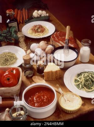 Verschiedene Nudelgerichte auf Tellern, umgeben von Zutaten auf einem alten Holztisch. Studiofoto, vertikal. Stockfoto