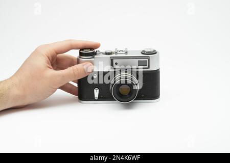 Hand drückt die Aufnahmetaste einer Oldtimer-Filmkamera, isoliert auf weißem Hintergrund. Hand fotografiert mit einer alten Filmkamera. Mit dem Finger auf drücken Stockfoto