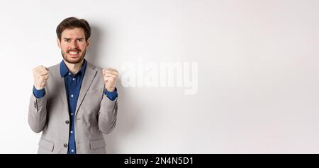 Angespannter Geschäftsmann, nervös und unter Druck, mit Fäusten und Zähnen, starrend auf die Kamera, Geld verdienen und besorgt aussehen, auf Weiß stehend Stockfoto