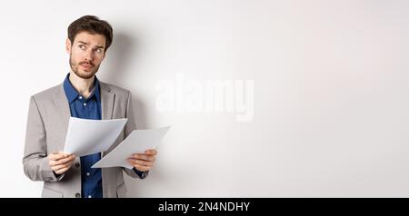 Geschäftsmann in Anzug durch Papiere suchen, Dokumente bei der Arbeit lesen und denken, Blick neben Logo, beschäftigt auf weißem Hintergrund stehen Stockfoto