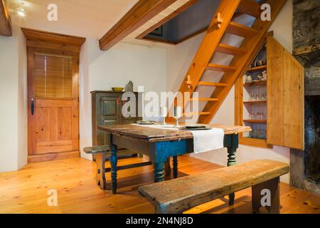 Antiker Kiefernholz-Schmetterlingstisch aus dem Jahr 1850er mit Zinngeschirr und Sitzbänken im Esszimmer Küchenbereich mit Steinkamin. Stockfoto