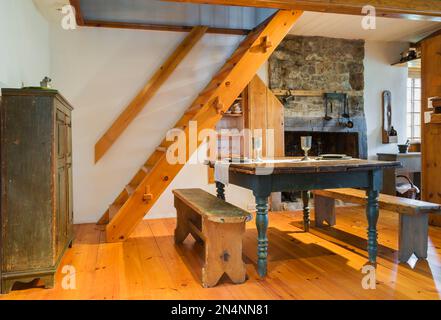 Antike Tannenholz Schmetterlingstisch aus den 1850er Jahren mit Zinn-Essgeschirr und Sitzbänken im Esszimmer, Küchenbereich mit Steinkamin. Stockfoto