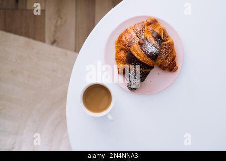 Eine Tasse Cappuccino und Croissants auf dem weißen Kaffeetisch im Zimmer Stockfoto