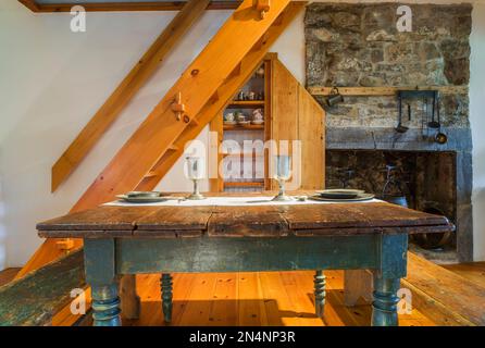 Antiker Kiefernholz-Schmetterlingstisch aus dem Jahr 1850er mit Zinngeschirr und Sitzbänken im Esszimmer Küchenbereich mit Steinkamin. Stockfoto