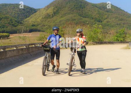 Asiatisches Fahrradpaar, das eine Pause vom Radfahren macht, macht eine Pause, geht spazieren und redet miteinander, um sich zu entspannen. Stockfoto