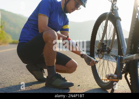 Asiatischer Radfahrer, der Luft in die Räder seines Fahrrads pumpt, um die Bereitschaft zu prüfen, bevor er morgens um den See fährt. Stockfoto