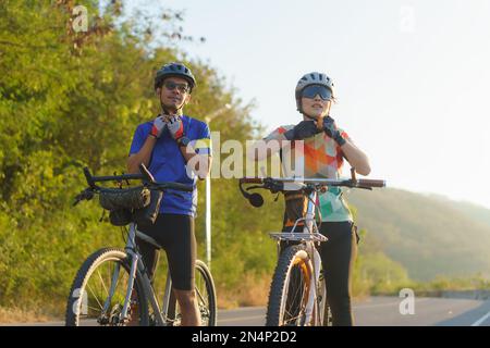 Asiatische Radfahrer, ein Paar Dons Helme und Kinnriemen, während sie sich auf ihre Fahrradtour um einen wunderschönen morgendlichen See vorbereiten. Stockfoto