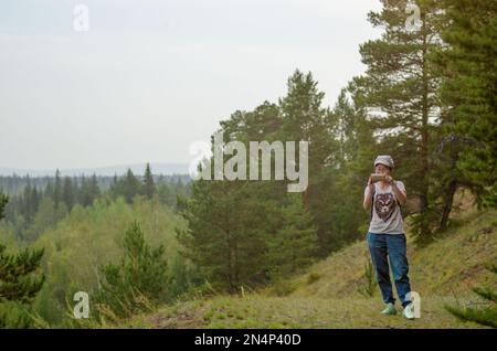 Yakut Asiatinnen-Tourist fotografiert am Telefon vom Berg im Fichtenwald von Nord-Yakutia mit Wald bis zum Horizont. Stockfoto