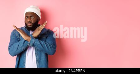 Enttäuscht Schwarzer Mann, starrte auf Kamera unzufrieden und runzelte die Stirn, zeigt Stop Cross Geste, verbieten und nicht einverstanden, stehen über rosa Hintergrund Stockfoto