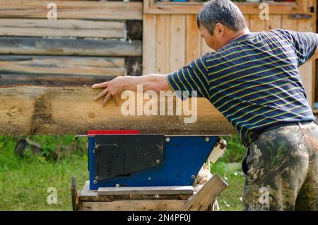 Ein erwachsener Yakut-Mann sägt ein Brett auf einer Säge gegen ein Holzhaus im Yakut-Dorf. Stockfoto
