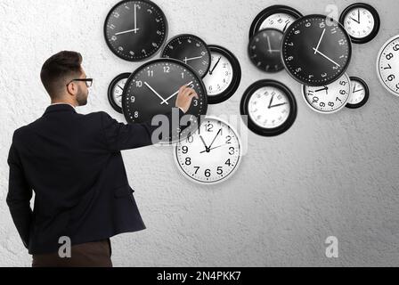 Zeitmanagementkonzept. Geschäftsmann und verschiedene Uhren auf hellgrauem Hintergrund Stockfoto