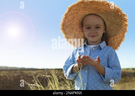 Süßes kleines Mädchen mit Strohhut im Freien, Platz für Text. Das Kind verbringt Zeit in der Natur Stockfoto