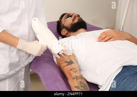 Junger Mann, der sich einer Lasertätowierung im Salon unterziehen muss Stockfoto