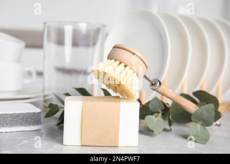 Reinigungsbürste und Seifenleiste zum Geschirrspülen auf grauem Marmortisch, Nahaufnahme Stockfoto