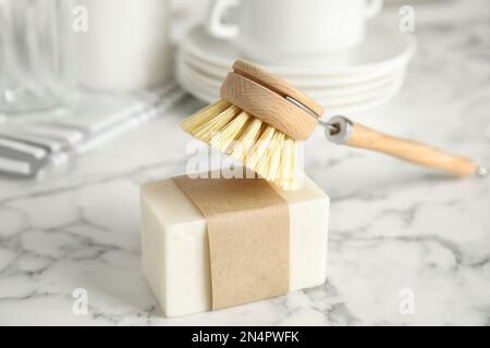 Reinigungsbürste und Seifenleiste zum Geschirrspülen auf weißem Marmortisch in Innenräumen, Nahaufnahme Stockfoto