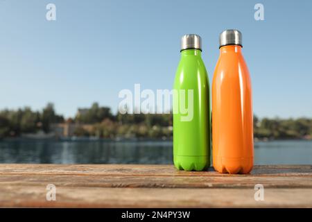 Moderne Thermosen auf Holzfläche in der Nähe des Flusses. Platz für Text Stockfoto