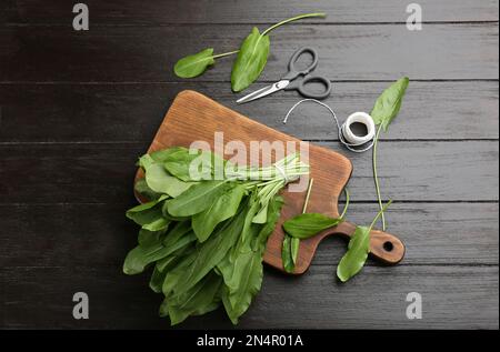 Frische grüne Sorrel-Blätter, Schere und Faden auf schwarzem Holztisch, flach liegend Stockfoto