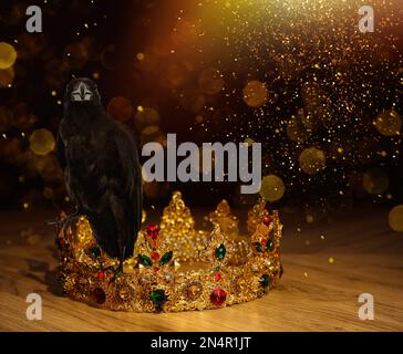 Fantasiewelt. Schwarze Krähe, beleuchtet von magischem Licht, auf goldener Krone, Bokeh-Effekt Stockfoto