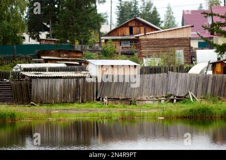 Hundewächter sitzt an einer Leine in der Nähe des Zauns mit den Häusern des Dorfes gegenüber dem Teich im nördlichen Yakut-Dorf Suntar. Stockfoto