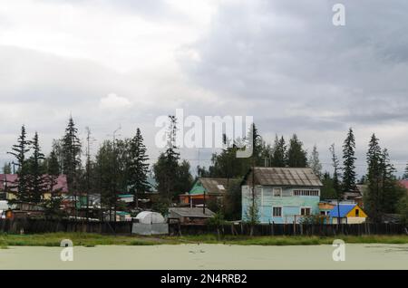 Private Häuser im nördlichen Fichtenwald des Dorfes ulus Suntar in Yakutia befinden sich in der Nähe eines schlammigen Sees. Stockfoto