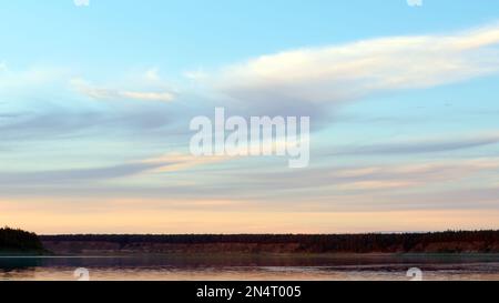 Heller, sanfter Sonnenuntergang am Ufer des nördlichen Flusses Vilyu unter dem Himmel mit Wolken und Klippen von Fichtentaiga in Yakutia mit Wellen aus dem wi Stockfoto